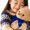 Child holding a teddy bear with a blue bow tie against a white background